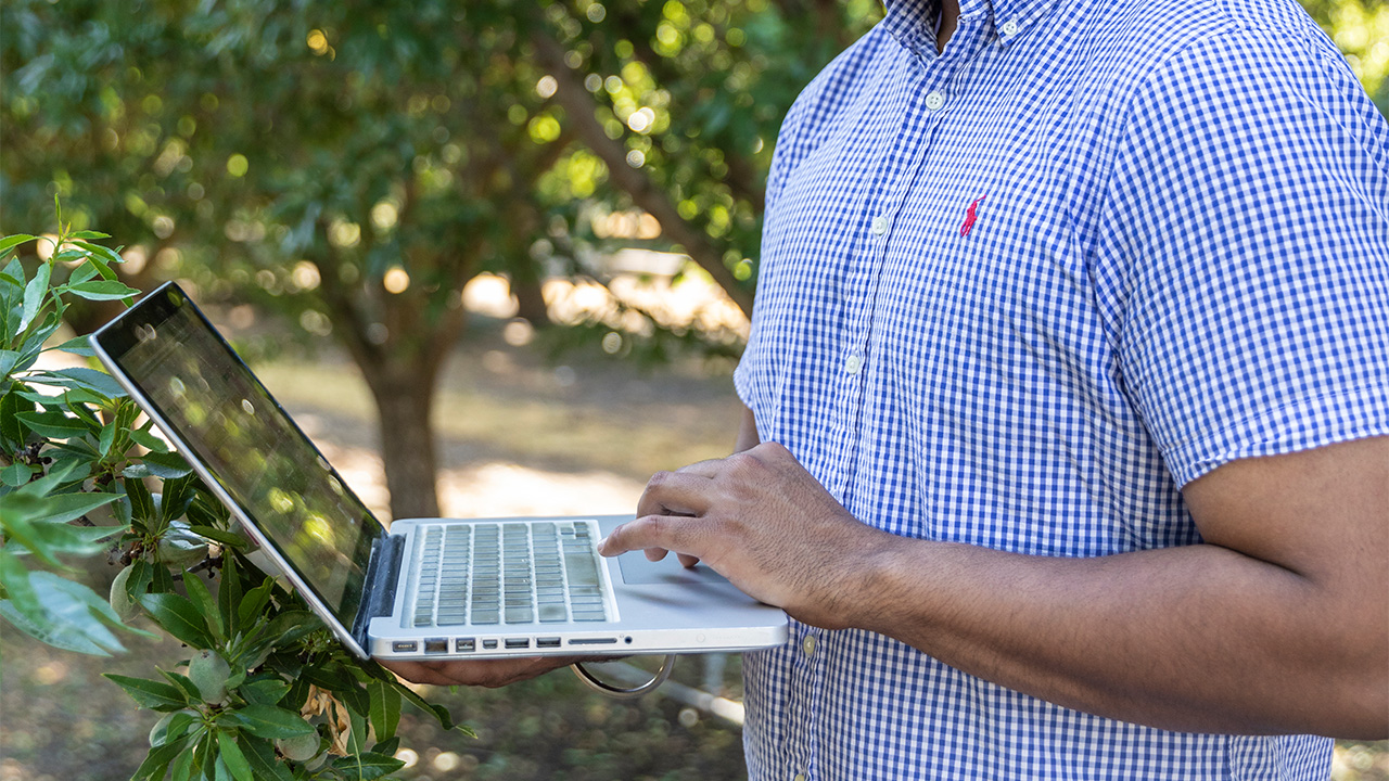 Grower Holding Laptop in Orchard