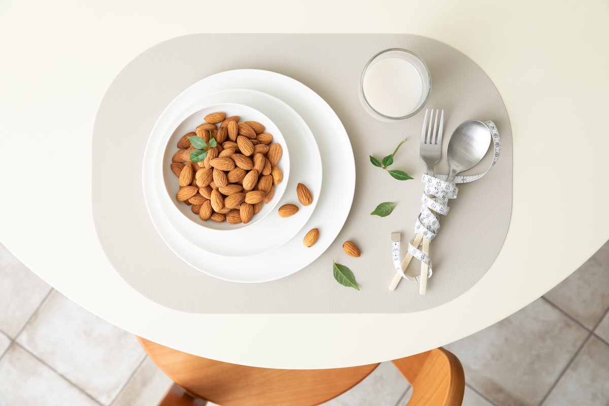 Almonds in a bowl next to utensils wrapped in tape measure